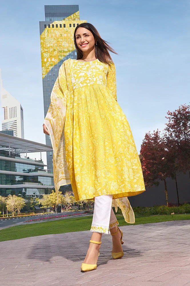 Model wearing a yellow Chikankari kurta with white pants and yellow sandals in a city park setting.